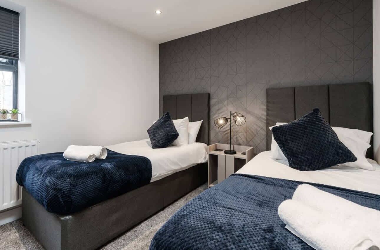 Ein Hotelzimmer mit zwei Betten, einem Nachttisch, einer Lampe und einem Fenster mit Jalousien.