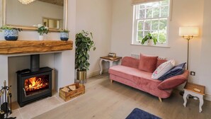 A cozy living room with a fireplace, a pink sofa, a large mirror, and a window with a view of greenery. - Beech (Newbury)