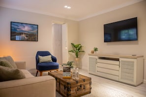 A living room with a sofa, a blue armchair, a wooden coffee table, a cabinet with a TV, and a painting on the wall. - Lovely 1BR in Miraflores (Lima)
