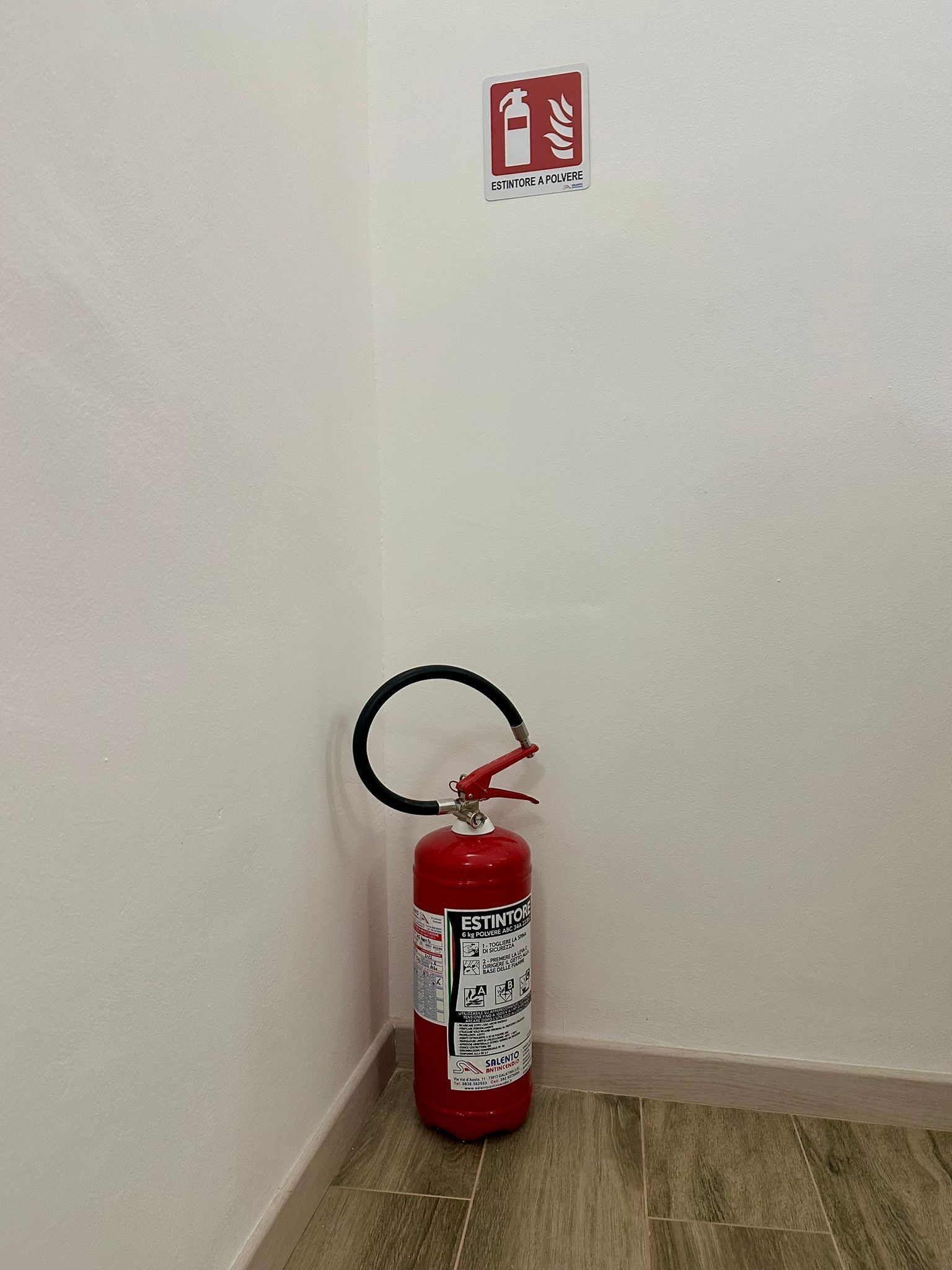 En brandslukker hængt på væggen i et hjørne, med et brandværnsur skilt over den.