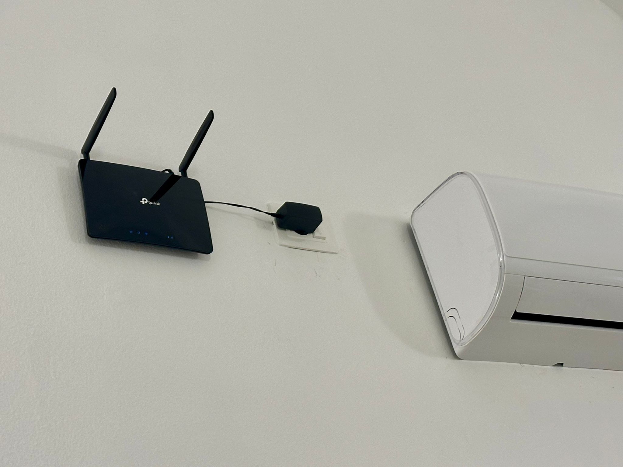 A wall-mounted router with two antennas and a power adapter plugged in.
