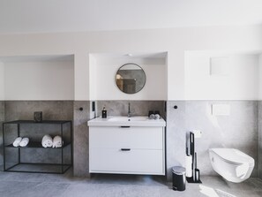 Une salle de bain moderne avec un meuble-lavabo blanc, un miroir rond et une étagère avec des serviettes.