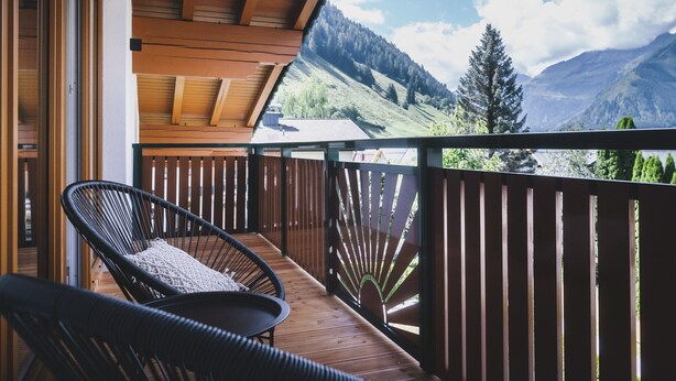 Een houten balkon met uitzicht op bergen en een stoel.