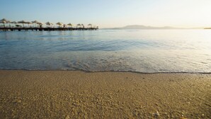 A beach with a calm sea, a sandy shore, and a pier with umbrellas. - Boyalık Beach Palms Hotel (Cesme)