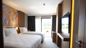 A hotel room with two beds, a TV, a desk, and a balcony with a view. - Boyalık Beach Palms Hotel (Cesme)