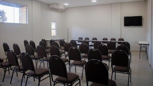 Ein Konferenzraum mit Reihen von Stühlen, einem großen Tisch, einer Projektionsleinwand und einem Flachbildfernseher an der Wand.