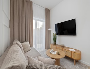 Una sala de estar moderna con un sofá, una mesa redonda de centro, un televisor montado en la pared y una ventana con cortinas.