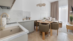 A modern kitchen with a built-in oven, a dining area with a round table and chairs, and a living area with a sofa and a TV. - Apartment, Indoor Pool, Close to the Beach (Rewal)
