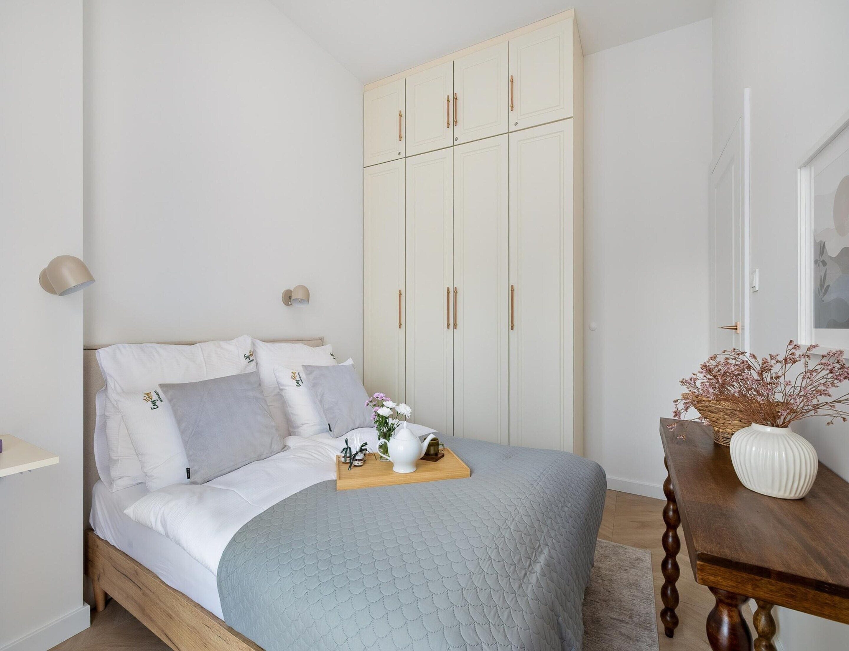 Ein Schlafzimmer mit einem Bett, einem Kleiderschrank, Nachttischlampen und einem Tisch mit einer Vase.