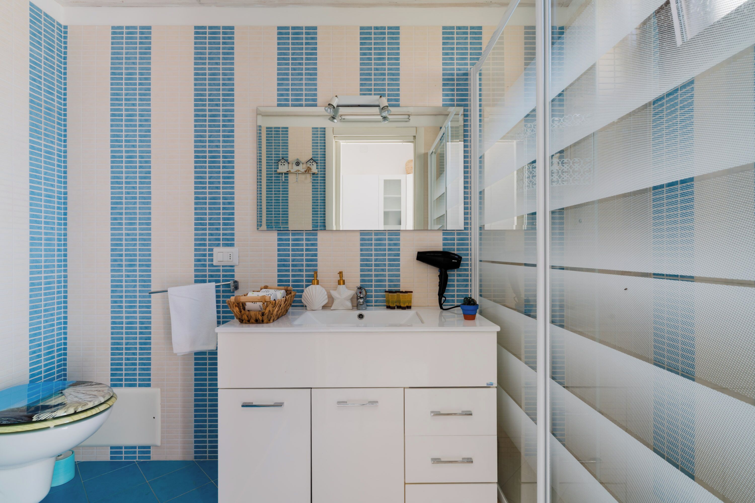 Un baño con lavamanos blanco, espejo y azulejos azul listados.