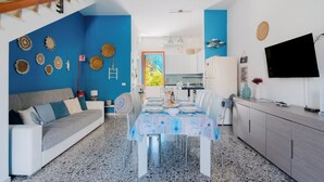 Una sala de estar moderna con una pared azul destacada, un comedor con una mesa dispuesta para cuatro personas y una cocina al fondo.