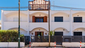 Un edificio de dos pisos con fachada blanca, múltiples ventanas con contraventanas y un balcón con barandilla de madera.