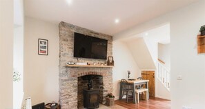 A living room with a stone fireplace, a flat-screen TV mounted above it, and a dining area with a wooden table and chairs.