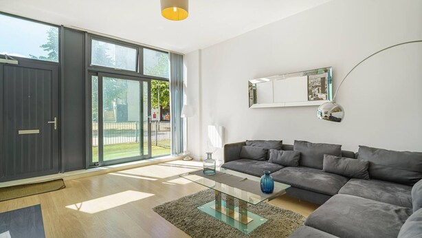 Una sala de estar moderna con un sofá gris, una mesa de centro de vidrio y un amplio ventanal corredero que da a un balcón.