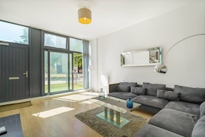 Uma sala de estar moderna com um sofá cinzento, uma mesa de centro de vidro e uma grande porta de correr que dá para uma varanda.