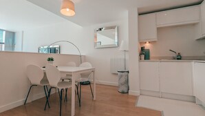 Una cocina moderna con armarios blancos, un comedor con mesa y sillas, y una lámpara colgante sobre la mesa.