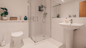 Un baño moderno con ducha de vidrio, lavamanos blanco y retrete.