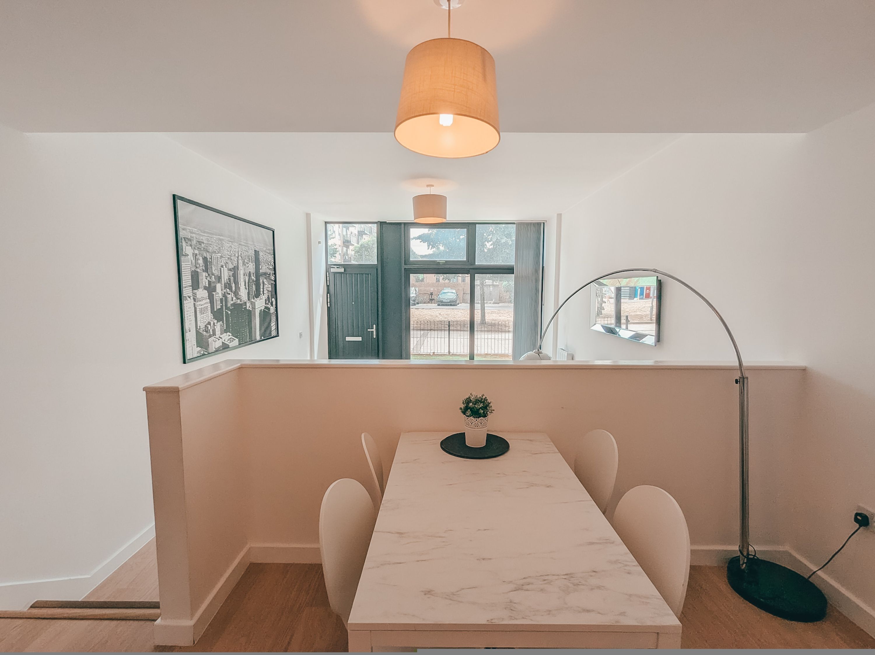 Un coin repas comprenant une table en marbre, des chaises, une suspension, un lampadaire, une fenêtre avec vue et un tableau encadré au mur.