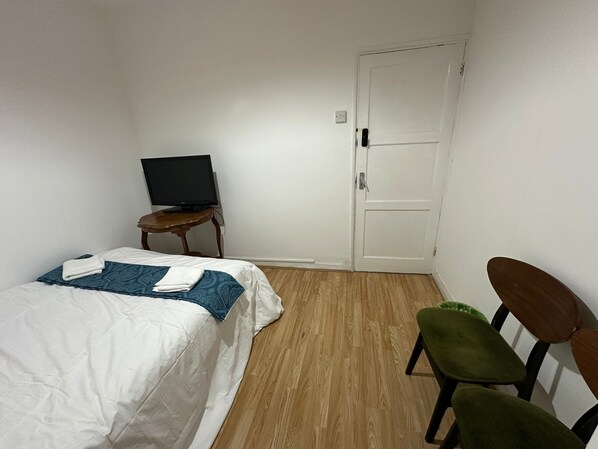 Una habitación de hotel con una cama, un televisor sobre una mesita y una puerta.