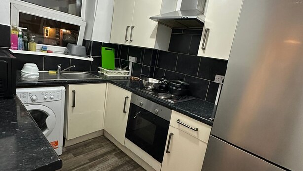 A modern kitchen with a stainless steel refrigerator, a built-in oven, a washing machine, and a window above the sink. - Comfortable Budget Room with Shared Bathroom in East London 2 (London)