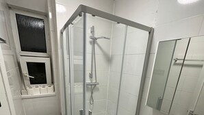 A small, modern bathroom with a glass-enclosed shower, a toilet, a sink, and a mirror. - Comfortable Budget Room with Shared Bathroom in East London 2 (London)