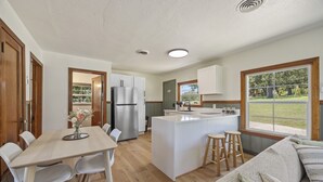 A modern kitchen with a central island, white cabinetry, and a dining area with a table and chairs.