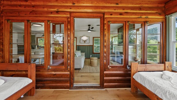 Un dormitorio tipo cabaña de madera con dos camas de madera, un ventilador de techo y ventanas amplias.