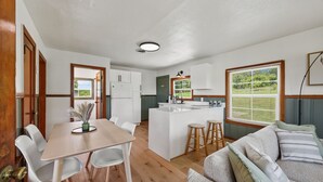 Una cocina moderna con armarios blancos, una isla central con taburetes y un comedor con mesa y sillas de madera.