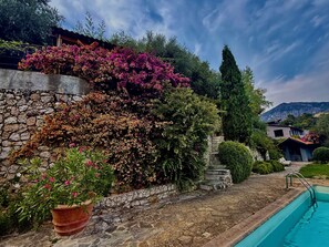 Eine Steinsäule mit blühenden Pflanzen, einem Pool und Blick auf die Berge.