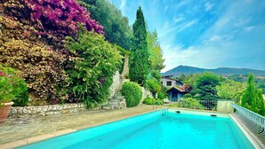 A swimming pool with a stone wall and lush greenery, a stone staircase, and a house in the background. - Spectacular4-bedroom Villa- Private Pool, Sea Views and TropicalGardens. (Menton)