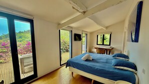 A bedroom with a large bed, a desk, and a view of a balcony with flowers. - Spectacular4-bedroom Villa- Private Pool, Sea Views and TropicalGardens. (Menton)