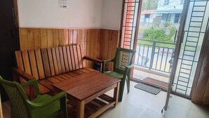 Un banco de madera con una mesa, sillas de plástico verde y vistas al exterior a través de un ventanal.