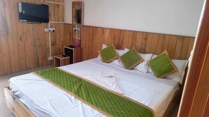 Habitación con paneles de madera, una cama, un televisor montado en la pared y una pequeña mesa con un objeto rosa.