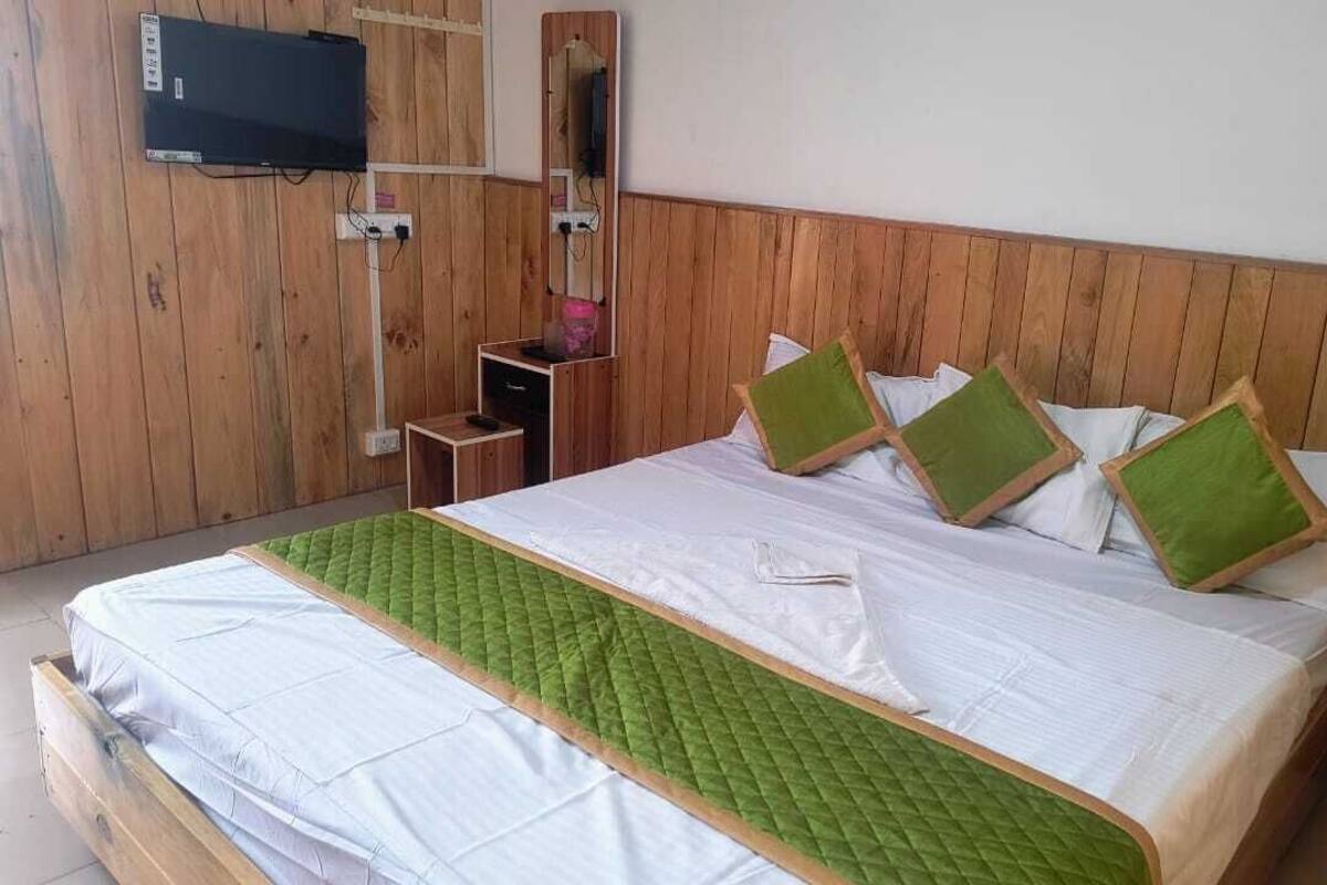 A wooden-paneled room with a bed, a TV mounted on the wall, and a small table with a pink object on it.