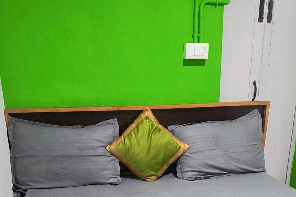 A bed with grey bedding, a red quilt, and a green pillow.