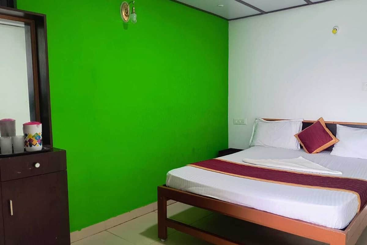 A bedroom with a green wall, a wooden bed frame, and a white mattress.