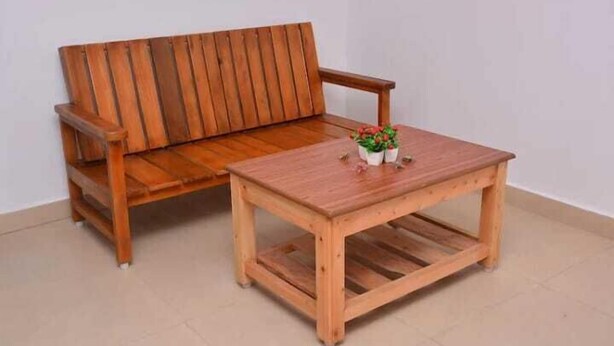 Un conjunto de sofá y mesa de madera en una habitación con pared blanca lisa y suelo de baldosas.