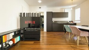 Una cocina moderna con horno integrado, un comedor con mesa y sillas, y una estantería con libros y objetos decorativos.