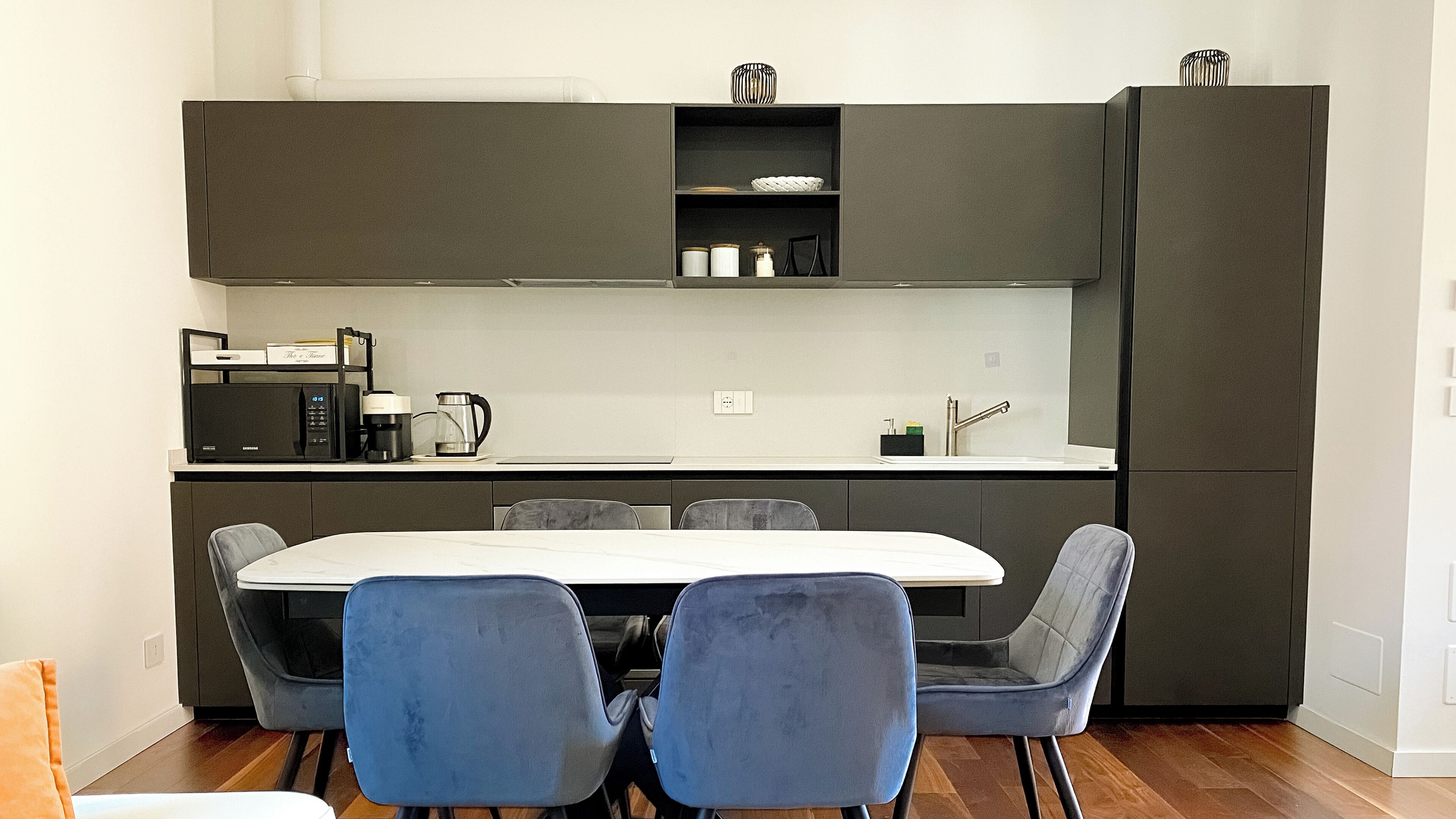 Una cocina moderna con armarios oscuros, una encimera blanca y una mesa de comedor con cuatro sillas.