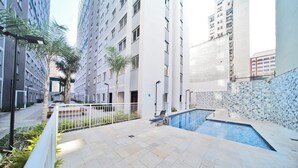 Un edificio residencial moderno con piscina, un patio cubierto y vistas de edificios altos cercanos.