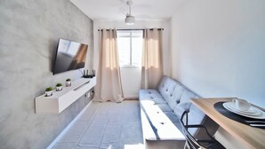 Una habitación moderna con sofá, televisor montado en la pared, una mesita con taza y plato, y un ventilador de techo.