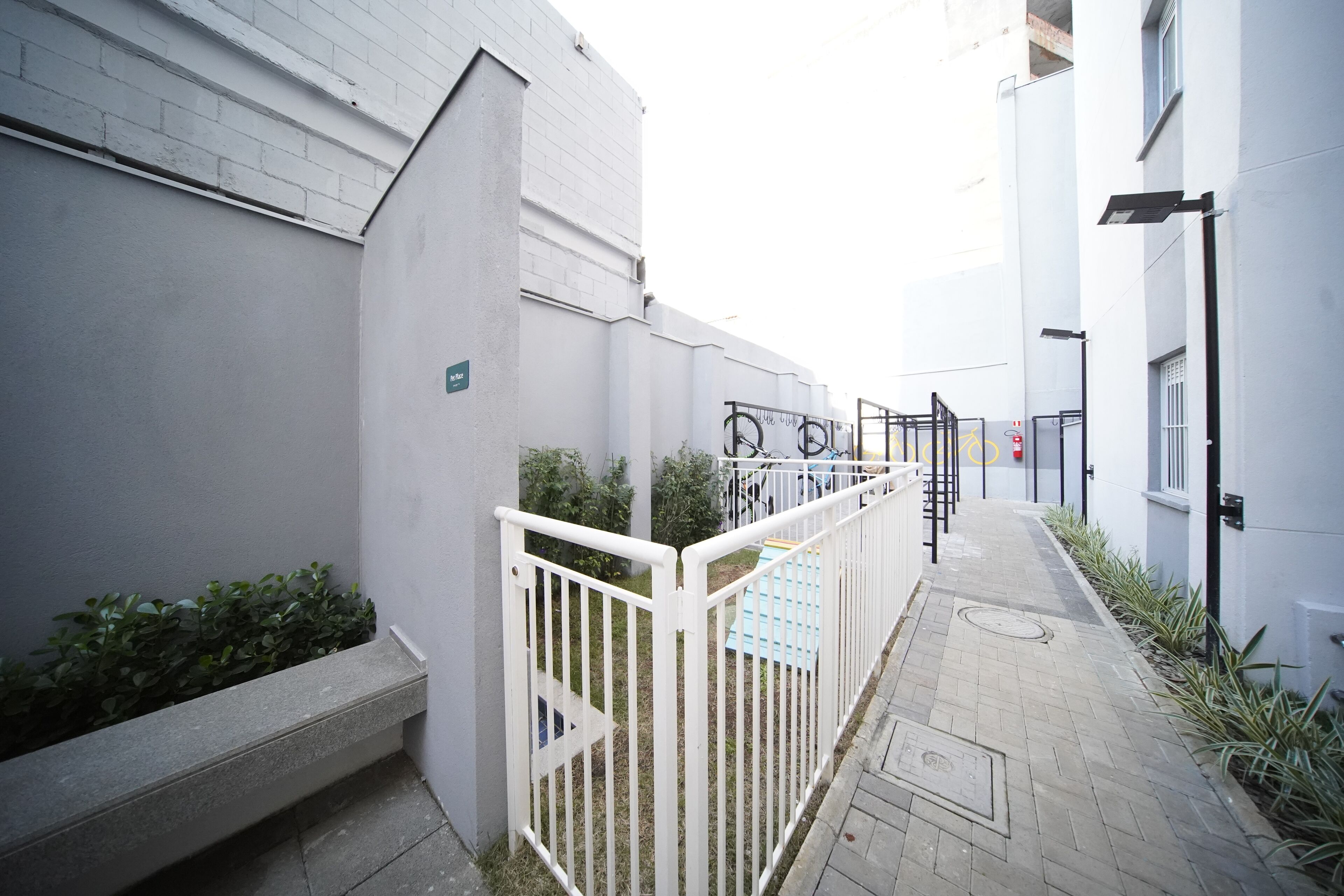 Un sendero estrecho bordeado por paredes blancas y una reja de metal, que conduce a la entrada de un edificio.