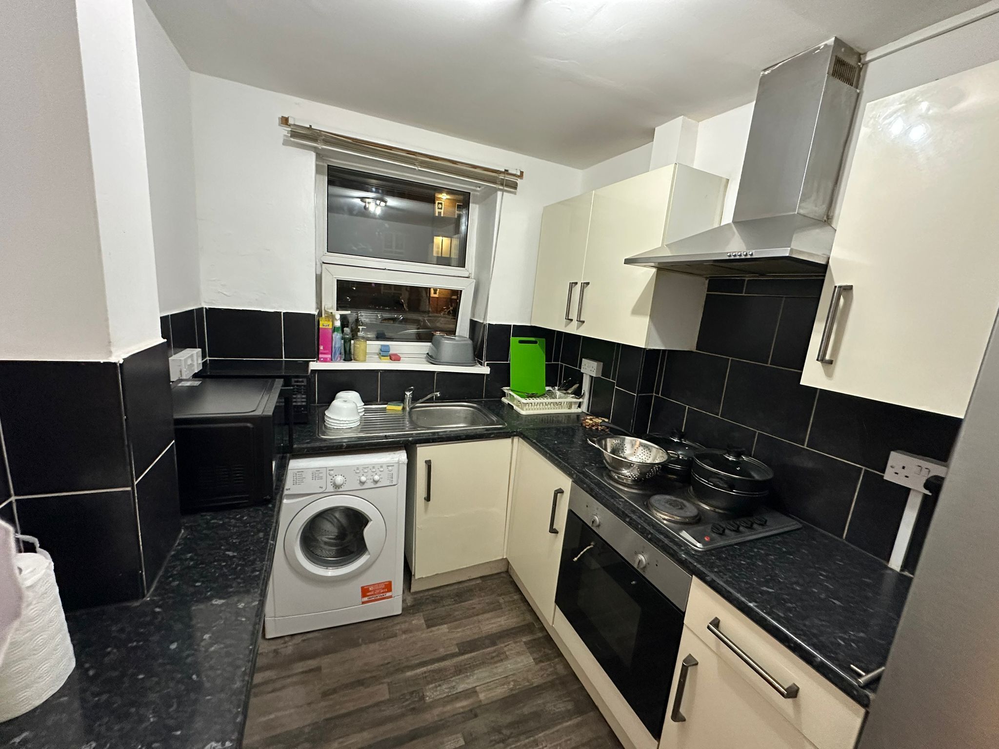 A compact kitchen with a washing machine, oven, and a window above the sink.