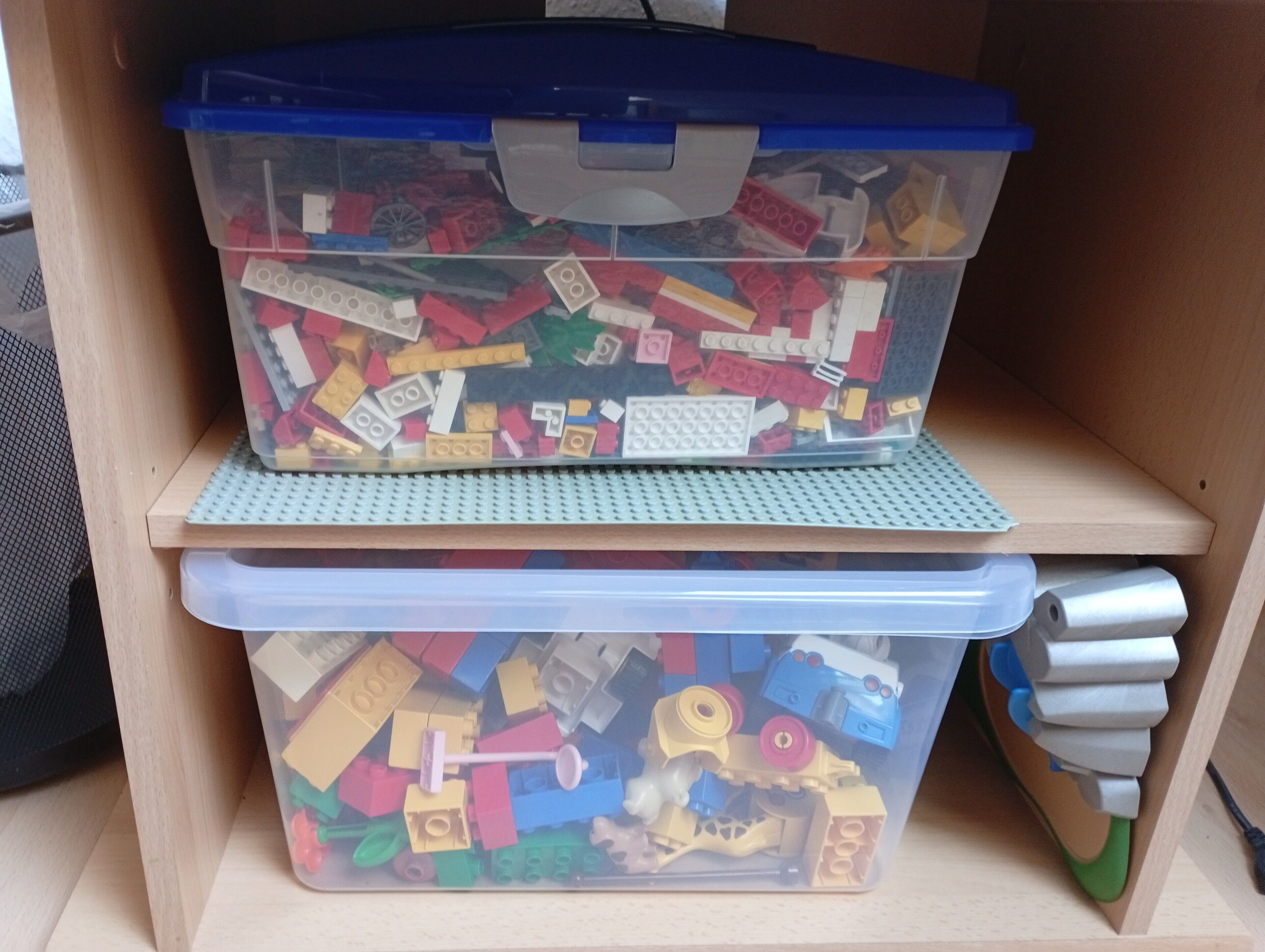 Deux bacs de rangement en plastique contenant des pièces de LEGO, placés sur une étagère en bois.