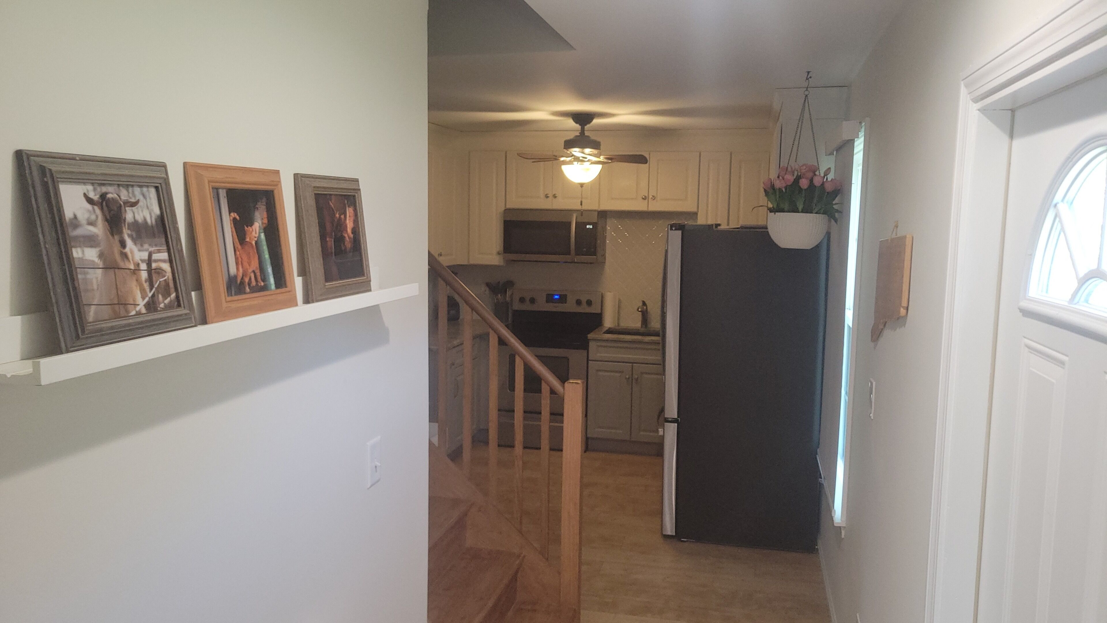 A hallway with a staircase, a kitchen area with cabinets and appliances, and a door with a window.