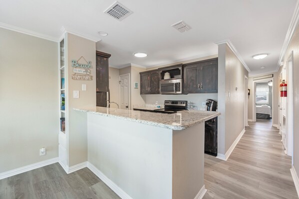 A modern kitchen with granite countertops, dark wooden cabinets, and a built-in microwave.