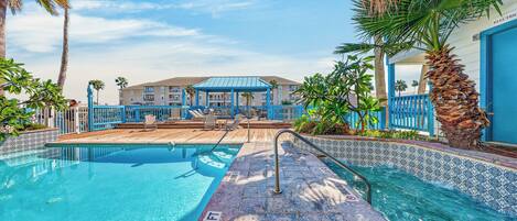 A swimming pool with a blue and white tiled edge, a wooden deck, and a building with a blue roof in the background.
