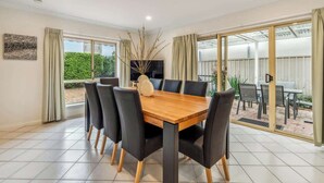 A dining area with a wooden table and black chairs, large windows, and a view of greenery outside. - Maison d'Art (Glenside)