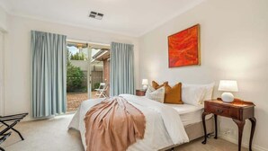 A bedroom with a bed, bedside tables, a window with curtains, and a painting on the wall. - Maison d'Art (Glenside)