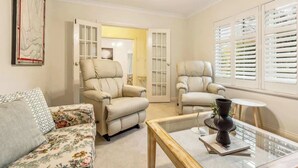 A living room with a sofa, two armchairs, a glass coffee table, and a door leading to another room. - Maison d'Art (Glenside)